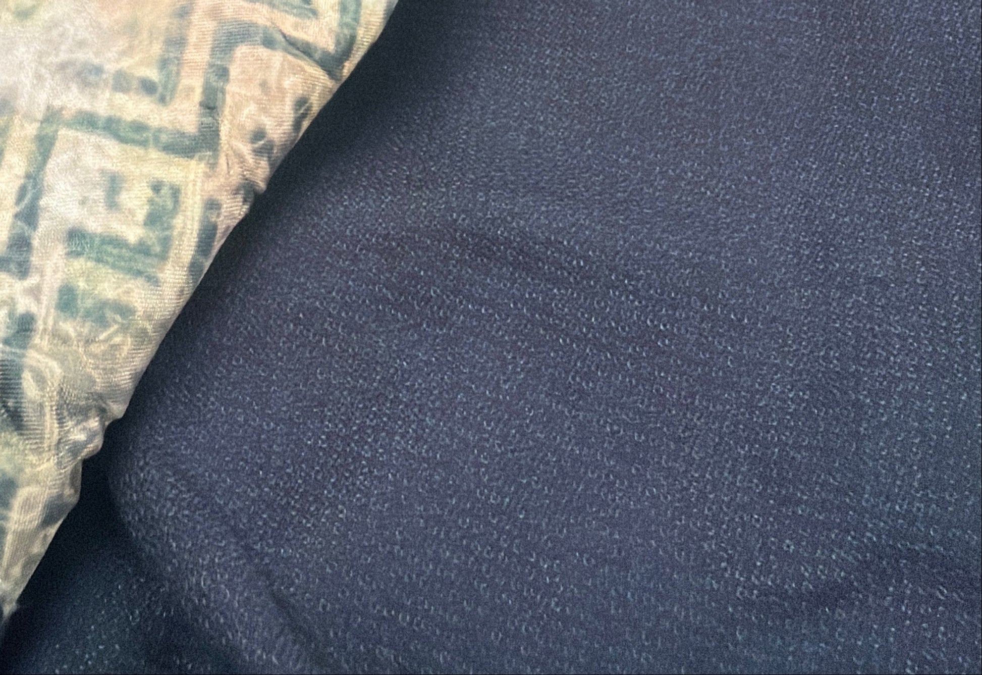A close-up of a folded navy blue garment, likely a kimono or traditional robe, featuring a patterned lining in beige, green, and blue, displayed on a hanger in a store setting.
