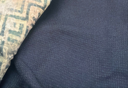 A close-up of a folded navy blue garment, likely a kimono or traditional robe, featuring a patterned lining in beige, green, and blue, displayed on a hanger in a store setting.