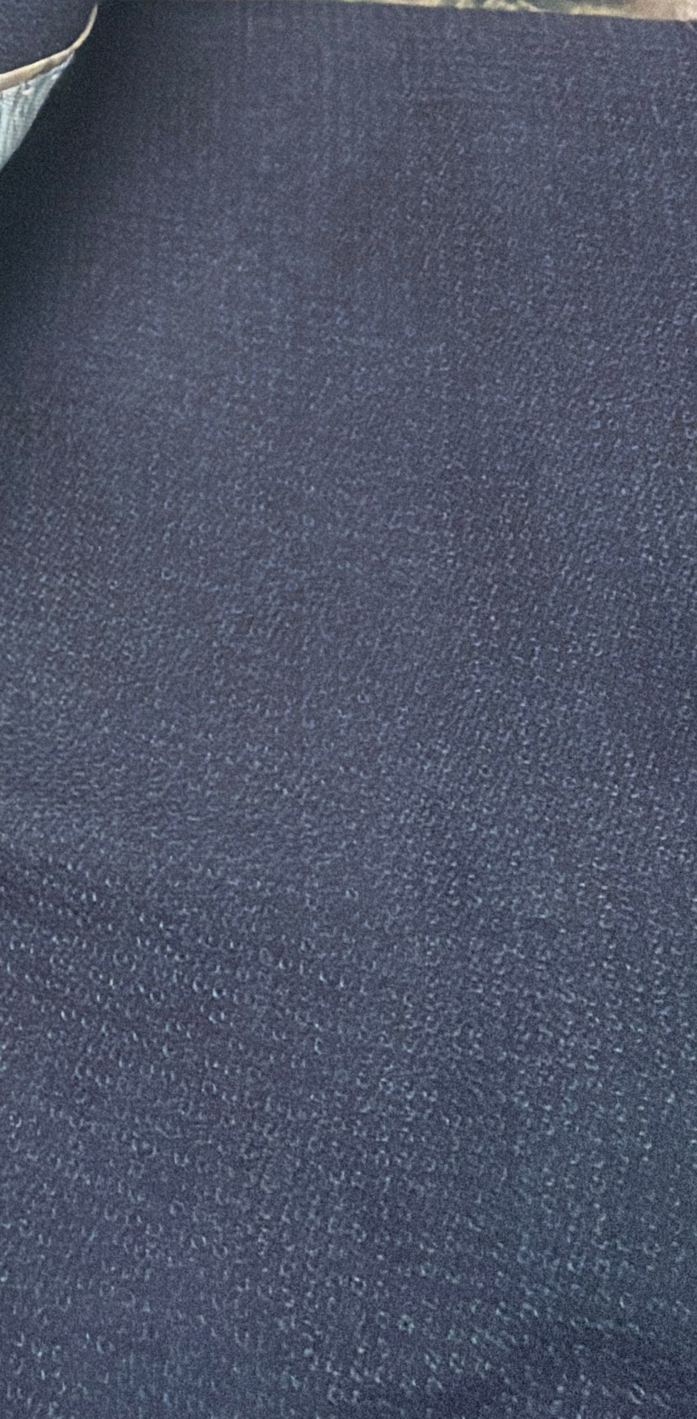 A close-up of dark navy blue textured fabric, showing a fine woven or knit pattern.

