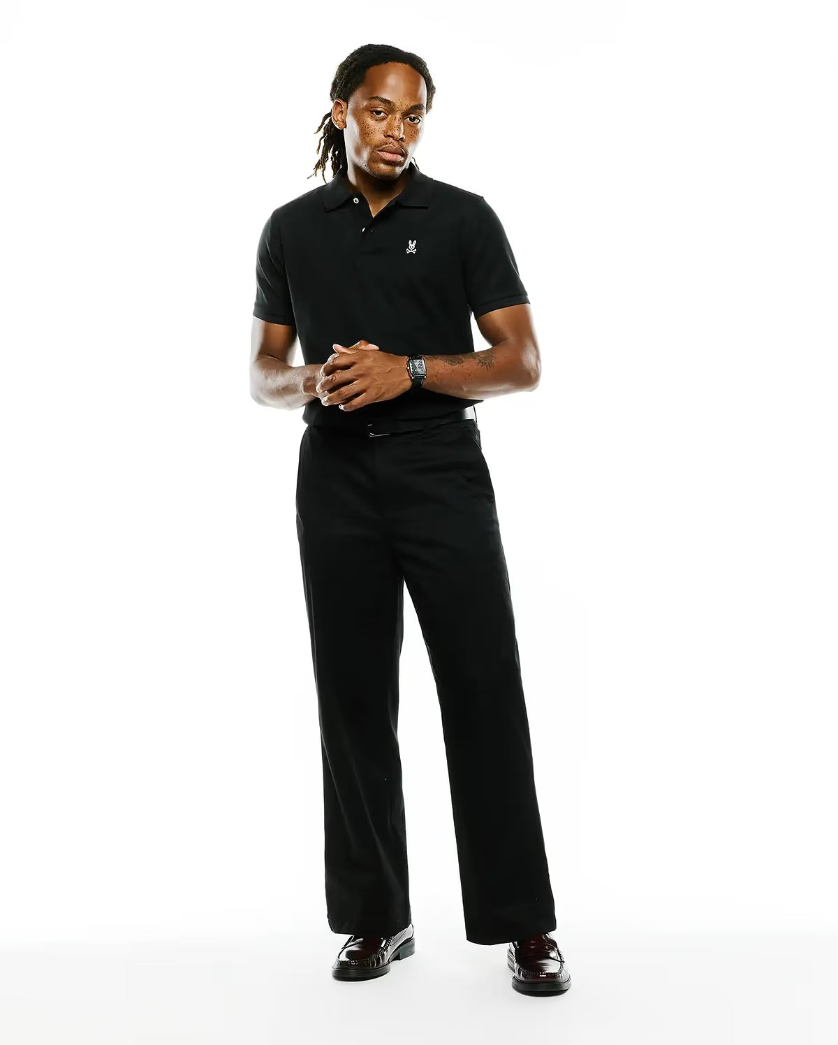 A man modeling a black short-sleeve polo shirt and matching black trousers against a plain white studio background.