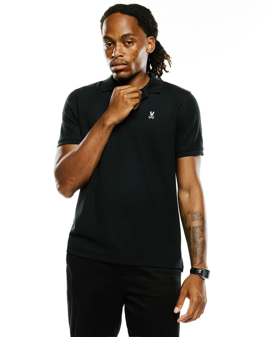 A man modeling a black short-sleeve polo shirt with a small white rabbit logo on the left chest, paired with black pants, against a solid white background.