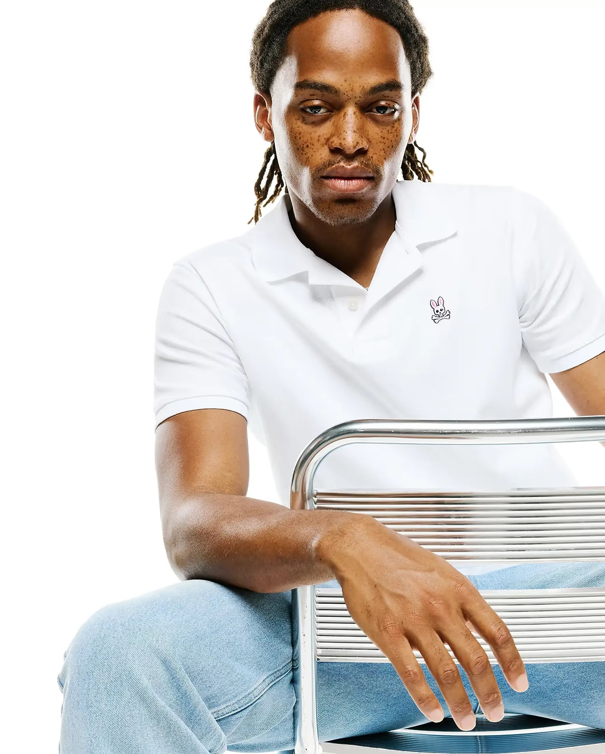 Seated model wearing Psycho Bunny men’s Classic Piqué Polo in white