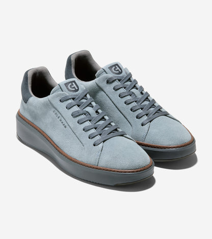 A pair of light blue suede low-top Cole Haan sneakers with dark gray laces, a thick dark gray sole, and a thin brown stripe detail on the side, shown against a light gray background.